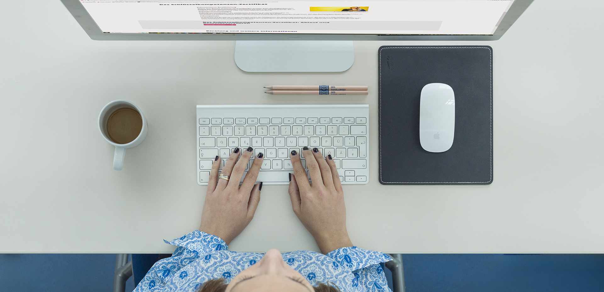 Frau am Schreibtisch mit Bildschirm, Maus, Tastatur und Kaffeetasse, dargestellt von oben